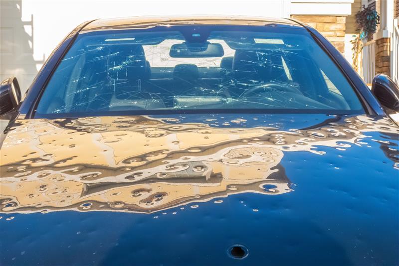 The front of a car displaying dents and cracks on the bonnet and windscreen due to hailstones.