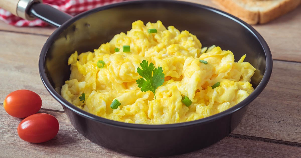 A pan full of cheesy scrambled eggs and herbs.