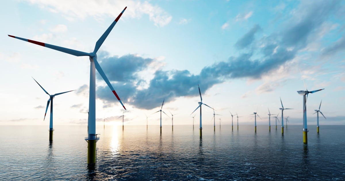 A row of wind turbines out on the ocean at sunrise.
