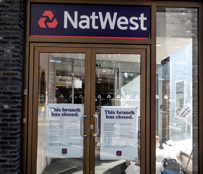 The front door of a NatWest bank, plastered with papers stating 'This branch is closing'.