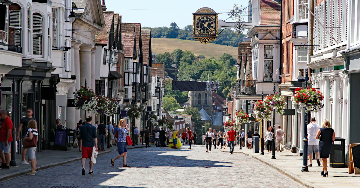 A traditional UK high street with crowds and cobbled stones.