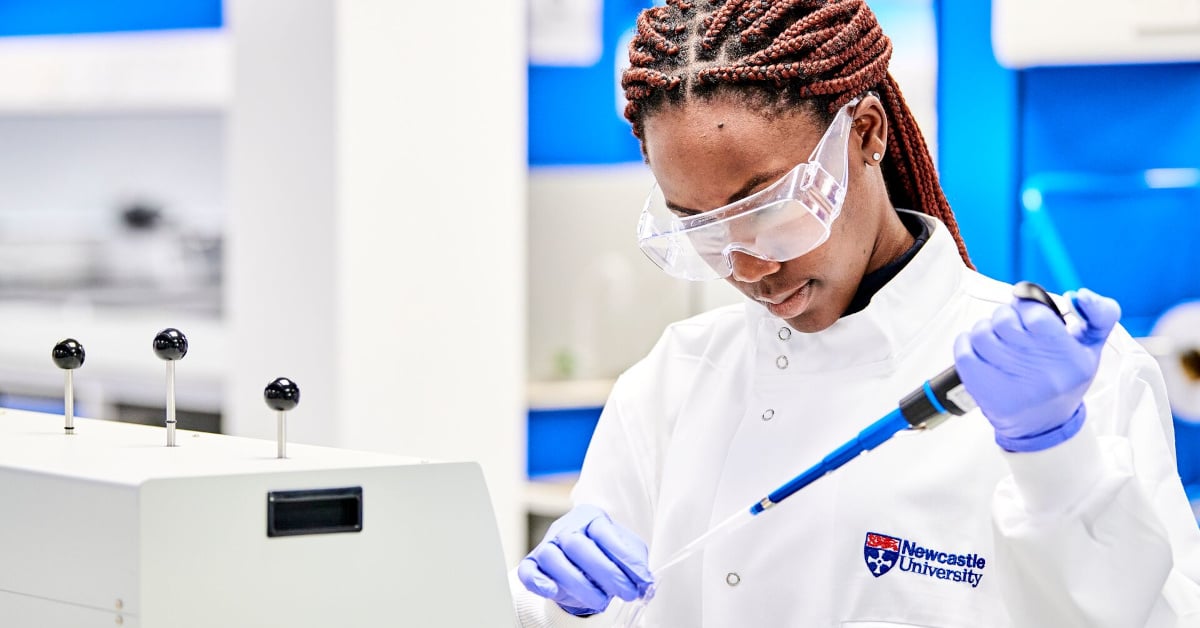 A Newcastle University student in lab equipment and safety glasses holds a pipette.