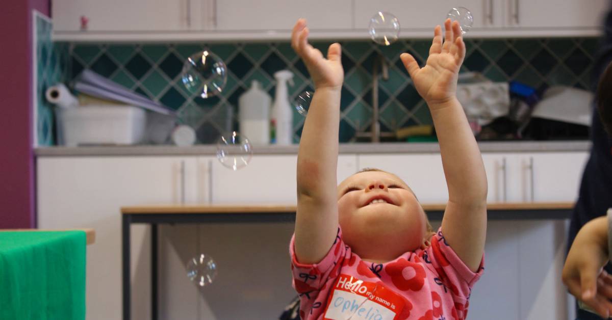 A toddler reaches for bubbles during a sensory play session at Babyzone Blackburn. Photo credit. Babyzone.