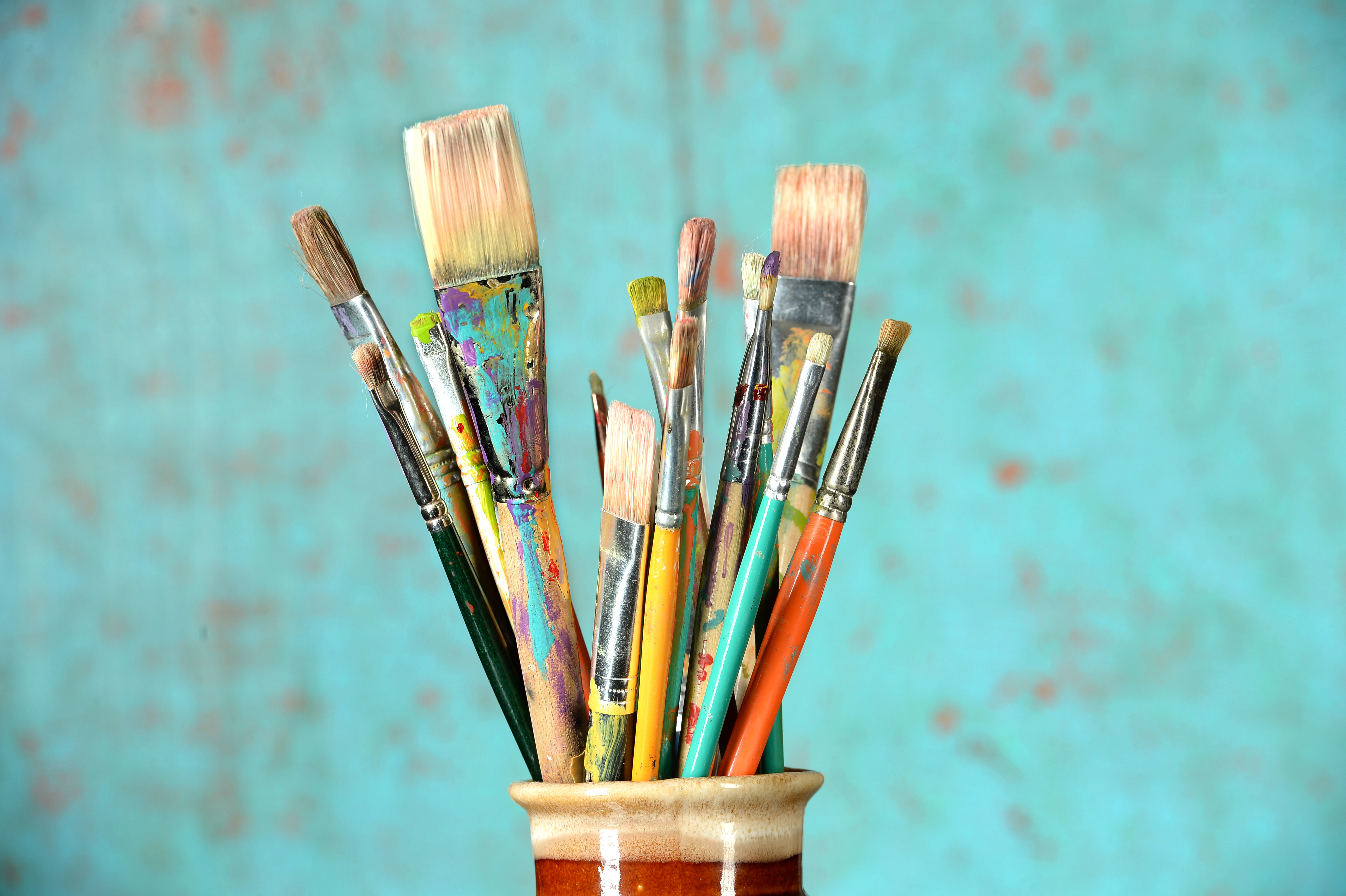 paintbrushes, covered with paint, stand against a blue background