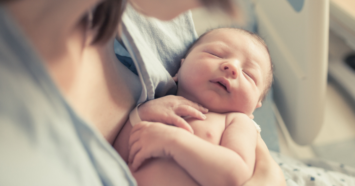 A newborn baby lying in their mother's arms.