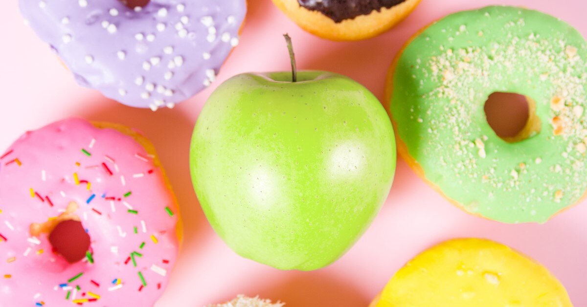 A green apple surrounded by iced doughnuts. 