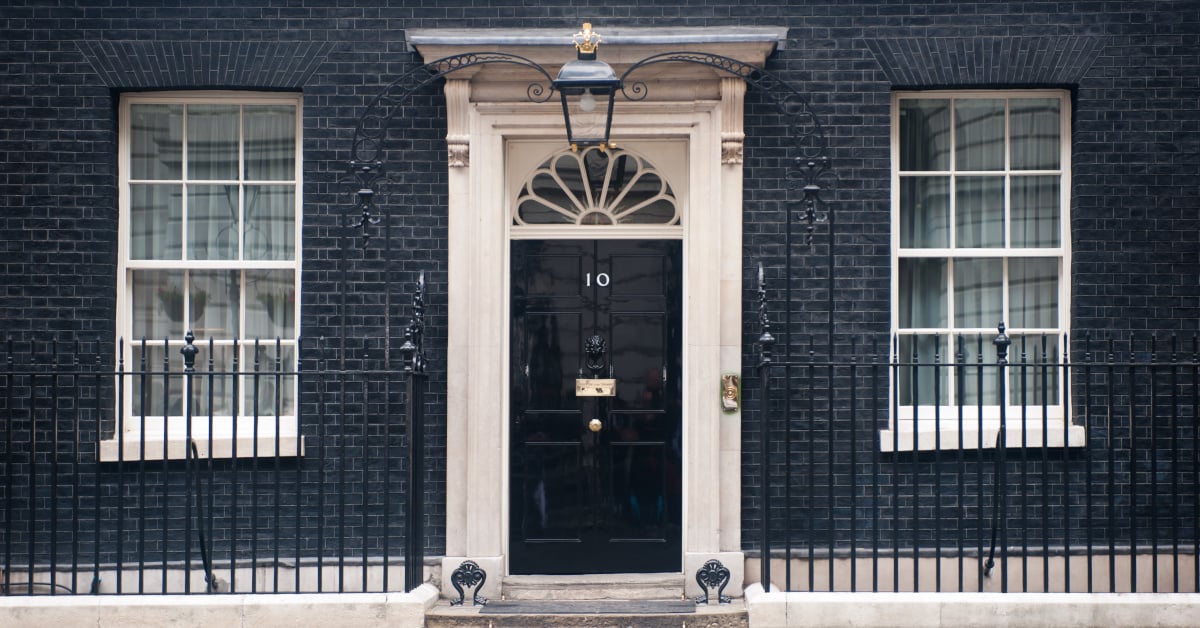 A photograph of 10 Downing Street in London: a black-bricked building and black door flanked with white pillars.