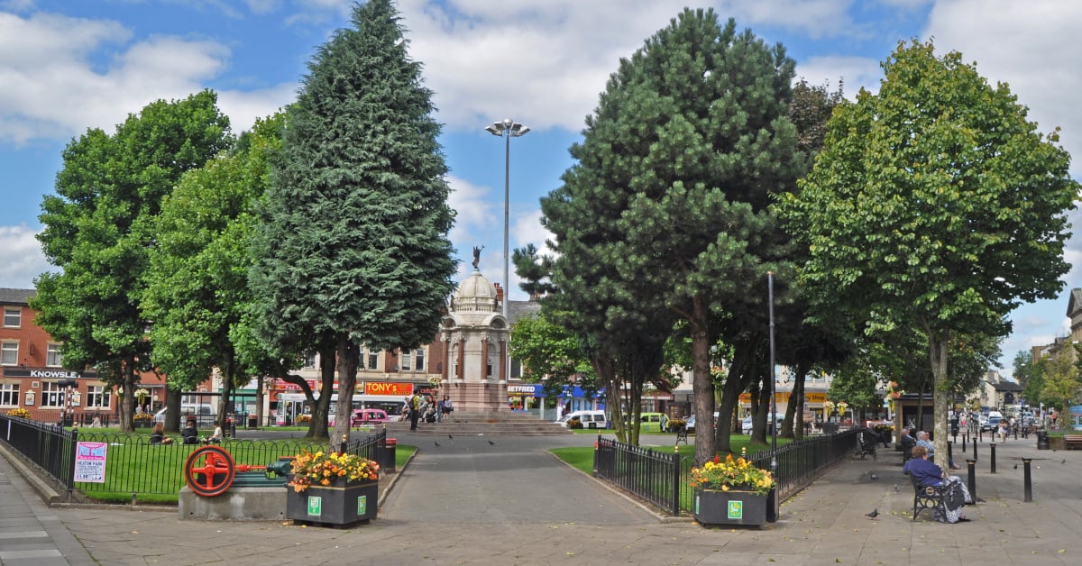 A town centre in Greater Manchester, UK, with a pathway bordered by picturesque trees.