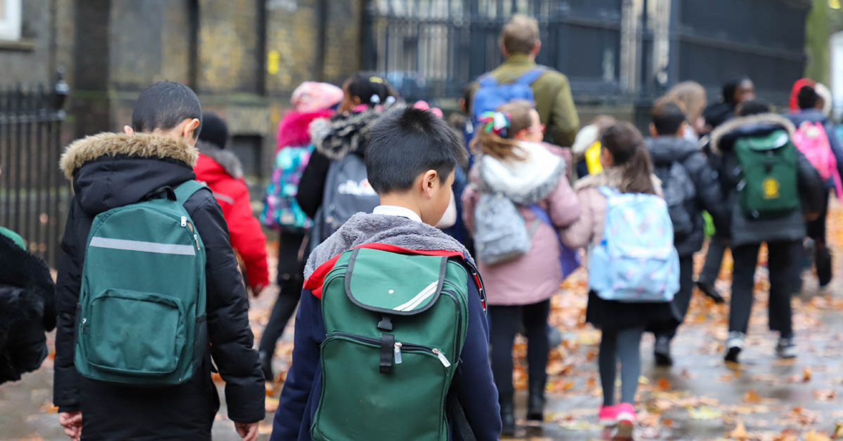 Primary school students and their teacher walk outside on a rainy day.