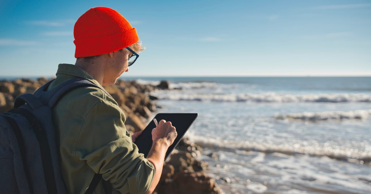 A marine biologist looks out to the ocean while working on a tablet.