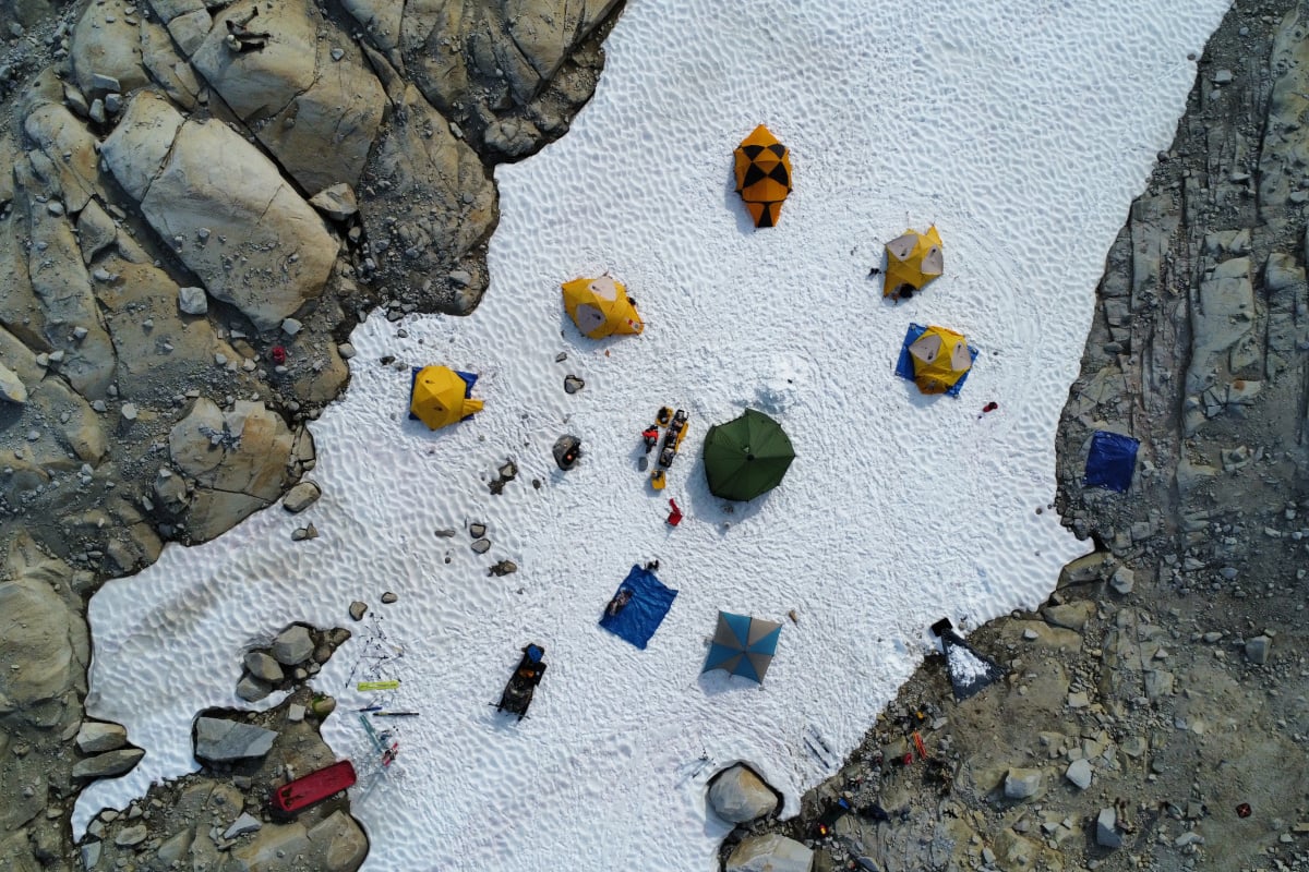 Researchers camp on the snow-covered ground around a glaciar - photo taken from above.
