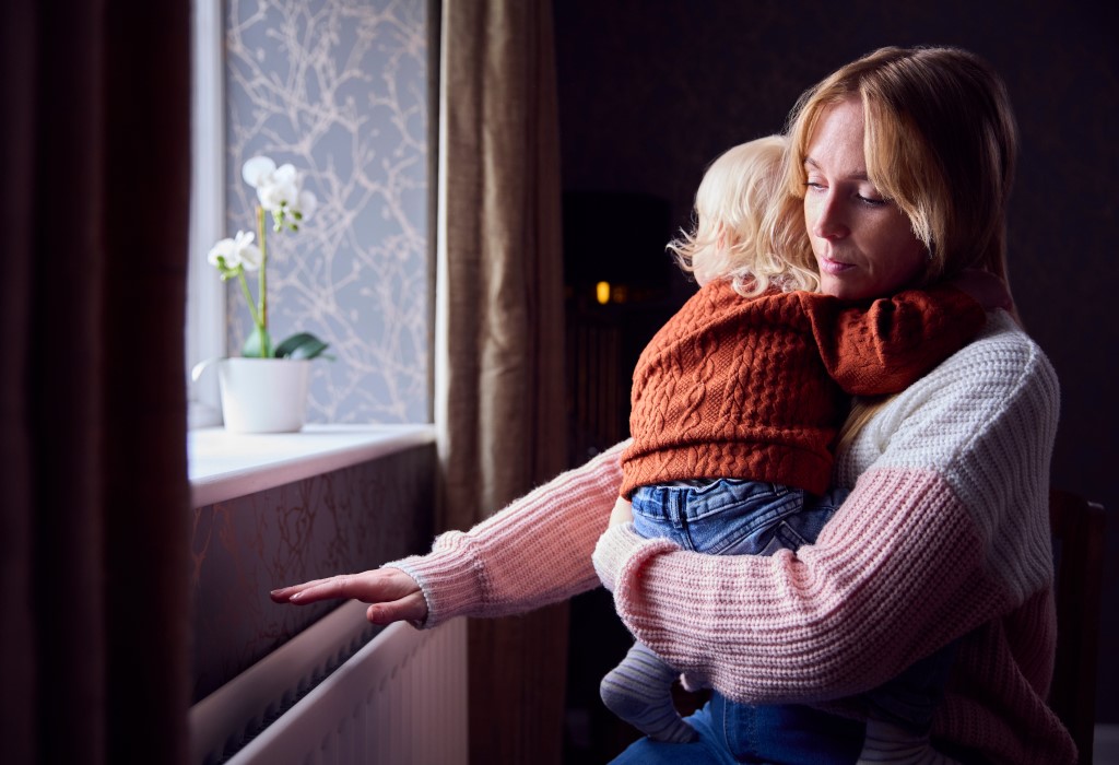 Woman holding child testing warmth of radiator