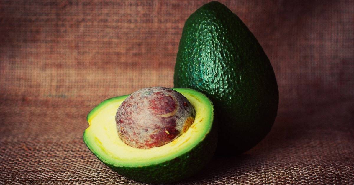 A sliced half of an avocado next to a whole avocado